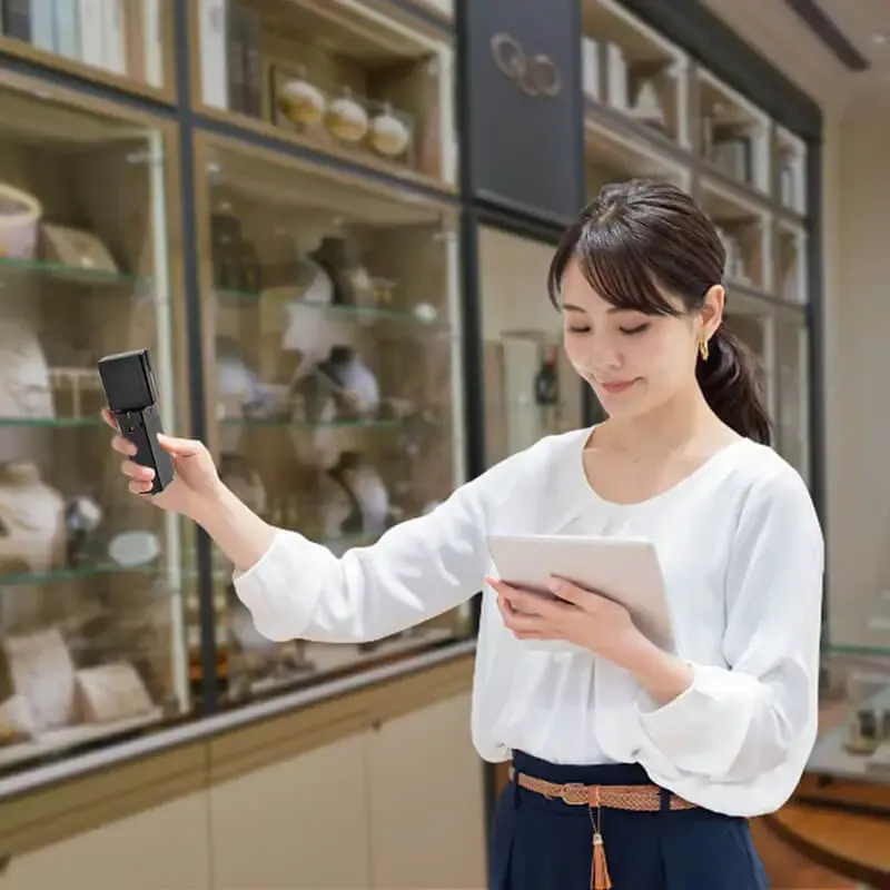 A woman using an RFID scanner and a tablet in a store with shelving displaying jewlery