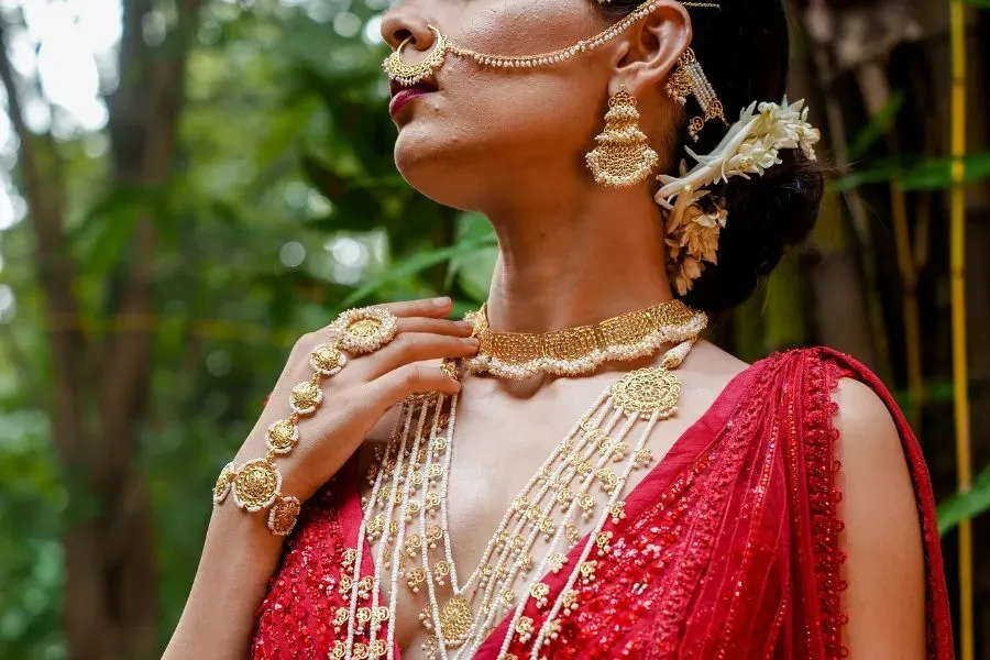 A woman wearing traditional gold Indian jewelry and a red saree, with flowers in her hair A woman wearing traditional gold Indian jewelry and a red saree, with flowers in her hair