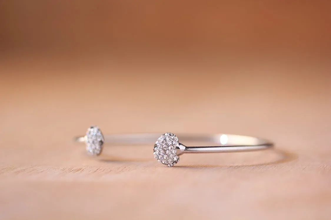 A bracelet with two small, round, diamond studded ends displayed on a wooden surface A bracelet with two small, round, diamond studded ends displayed on a wooden surface
