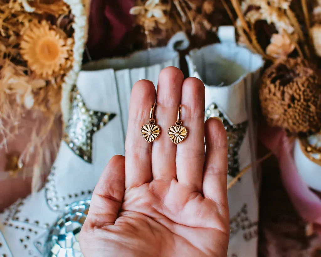 A hand holding a pair of gold heart shaped earrings with a decorative pattern A hand holding a pair of gold heart shaped earrings with a decorative pattern