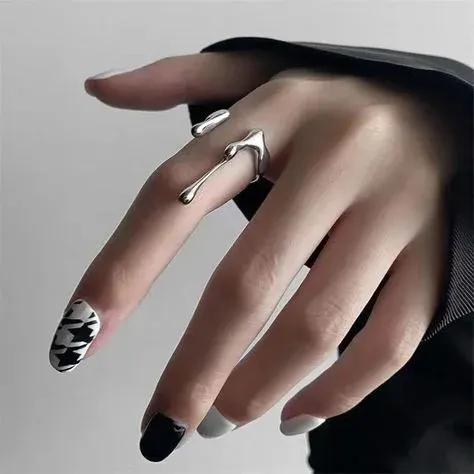 A hand with black, white, and patterned nails wearing a silver, abstract designed ring A hand with black, white, and patterned nails wearing a silver, abstract designed ring
