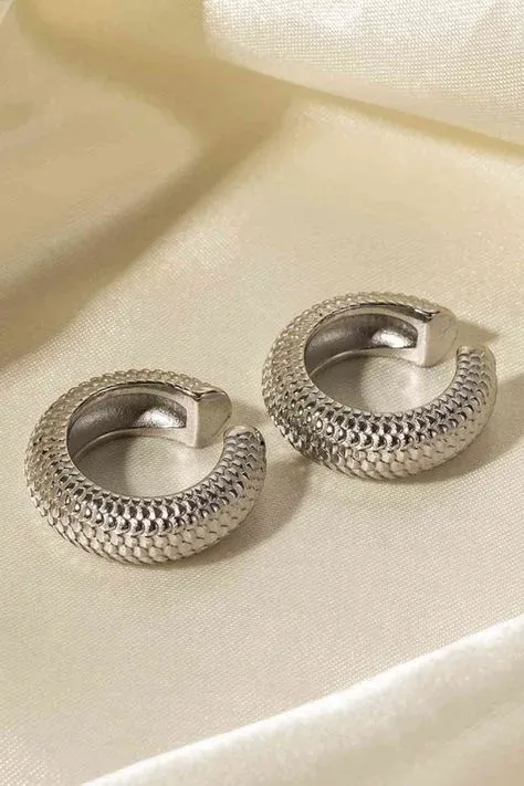 A pair of textured hoop earrings displayed on a cream colored fabric A pair of textured hoop earrings displayed on a cream colored fabric