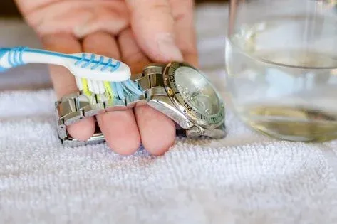 A person cleaning a silver wristwatch with a toothbrush A person cleaning a silver wristwatch with a toothbrush