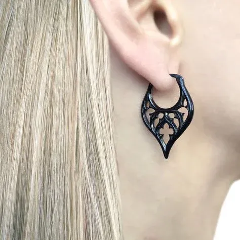 A person wearing a black, intricately designed earring with long blonde hair visible A person wearing a black, intricately designed earring with long blonde hair visible
