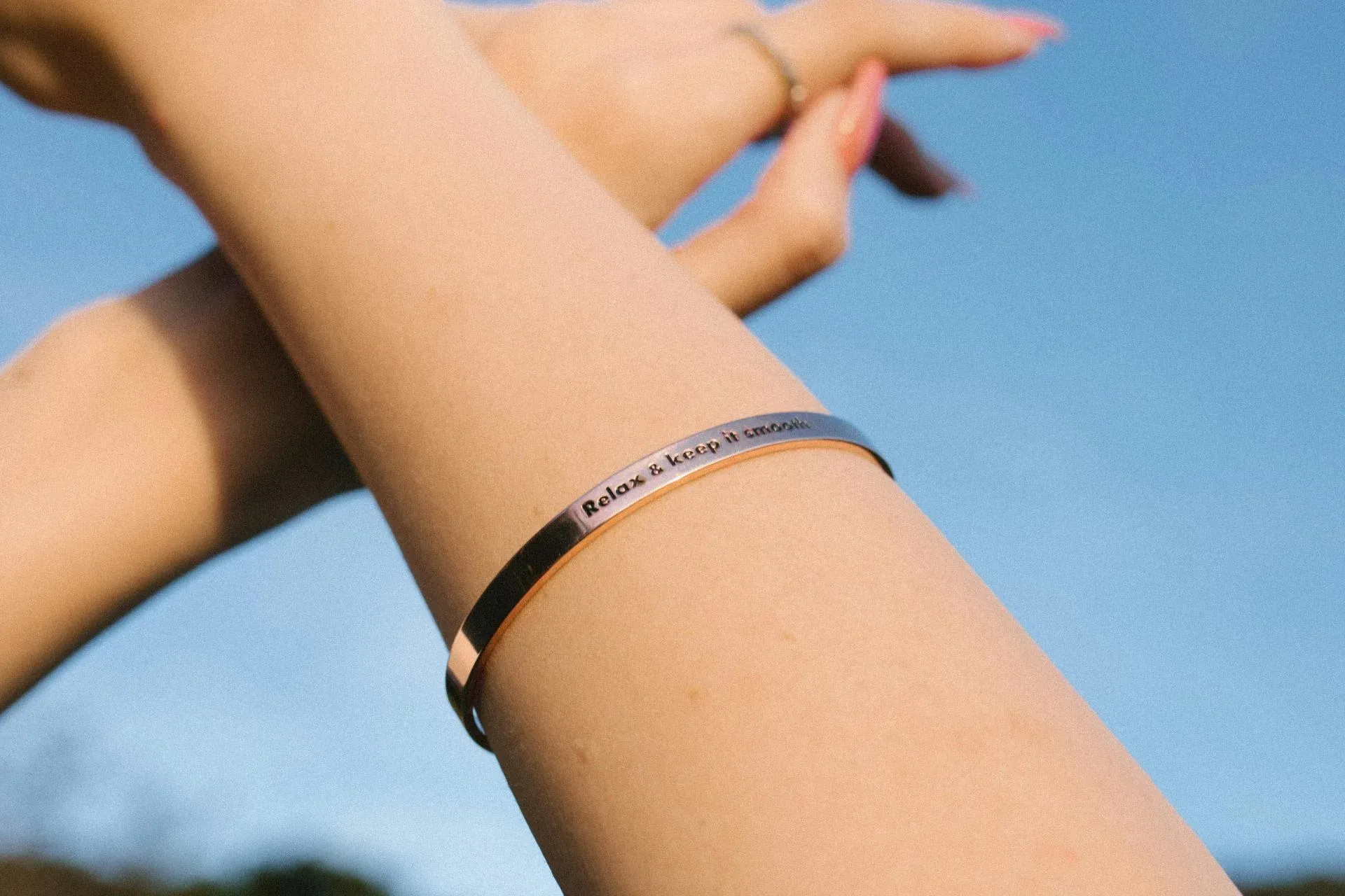 A person wearing a bracelet with arms raised against a blue sky A person wearing a bracelet with arms raised against a blue sky