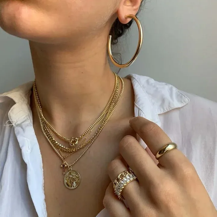 A person wearing gold hoop earrings, layered necklaces, and rings A person wearing gold hoop earrings, layered necklaces, and rings