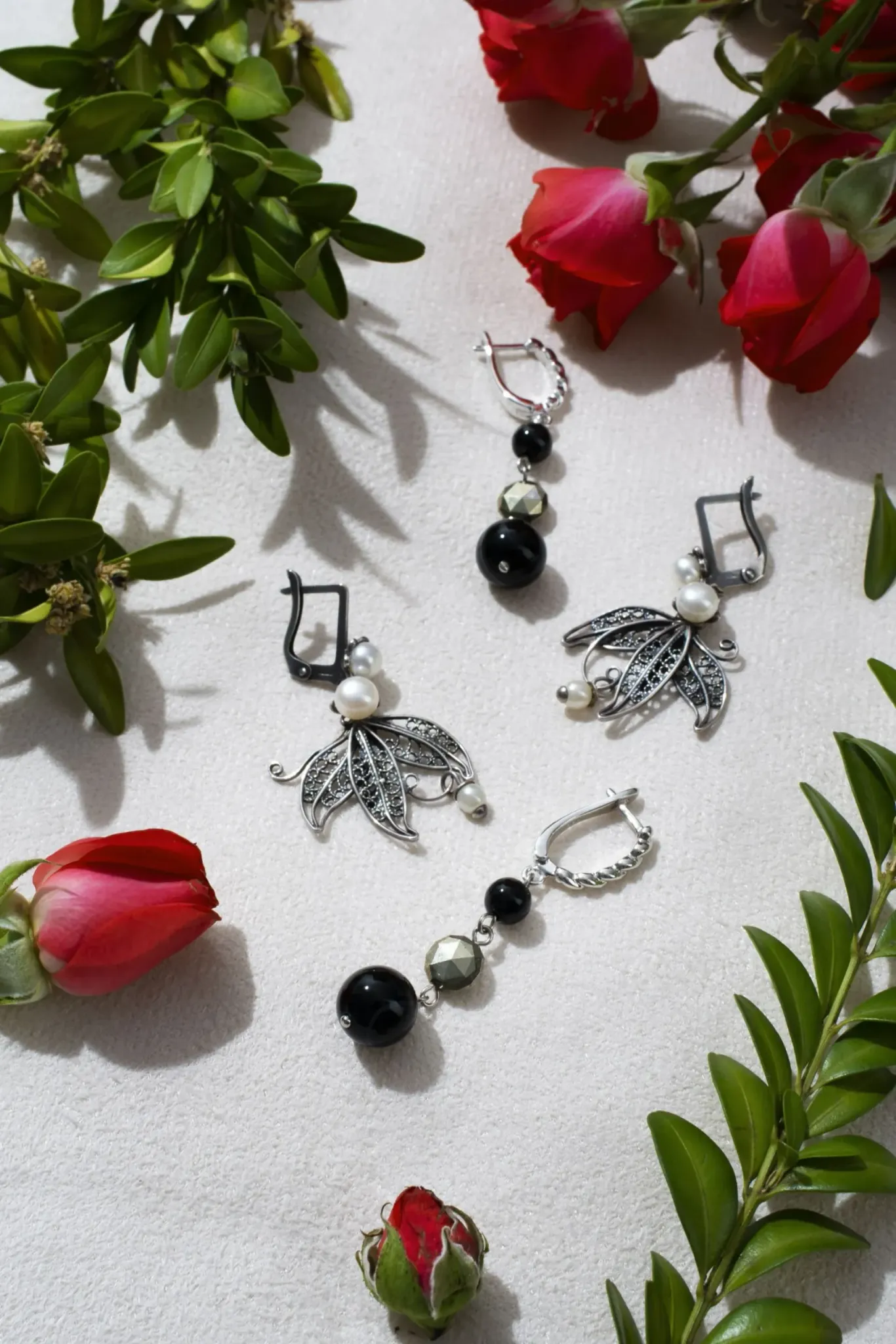 Assorted earrings with beads and crystals displayed among red roses and green leaves on a textured surface Assorted earrings with beads and crystals displayed among red roses and green leaves on a textured surface