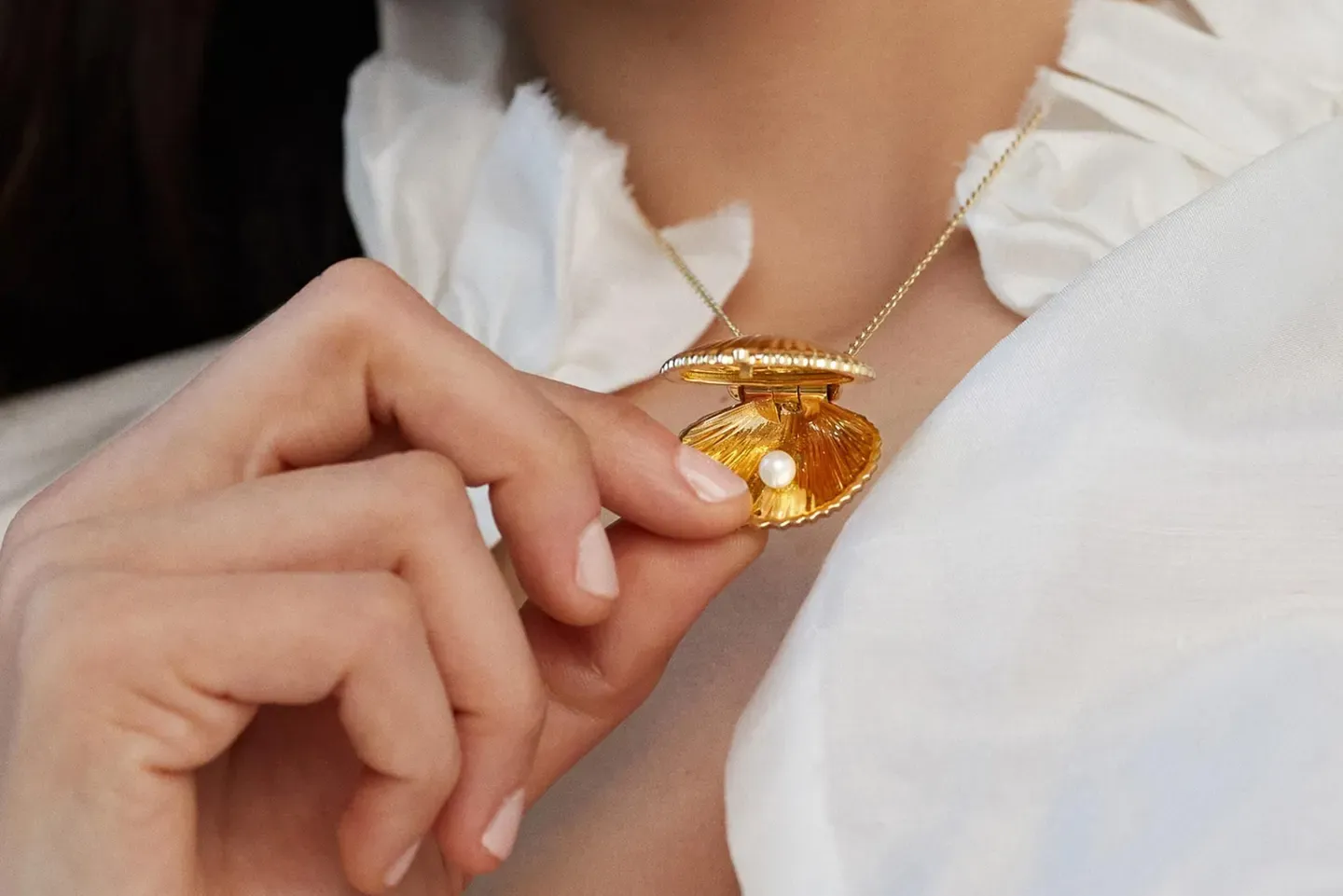 Close up of a woman's hands adjusting a golden shell shaped pendant with a pearl Close up of a woman's hands adjusting a golden shell shaped pendant with a pearl