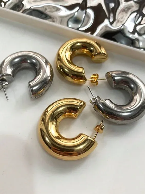 Four chunky hoop earrings on a white surface, two in shiny silver and two in glossy gold Four chunky hoop earrings on a white surface, two in shiny silver and two in glossy gold