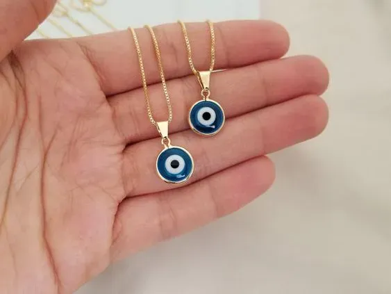 Hand holding two gold necklaces with blue and white evil eye pendants Hand holding two gold necklaces with blue and white evil eye pendants