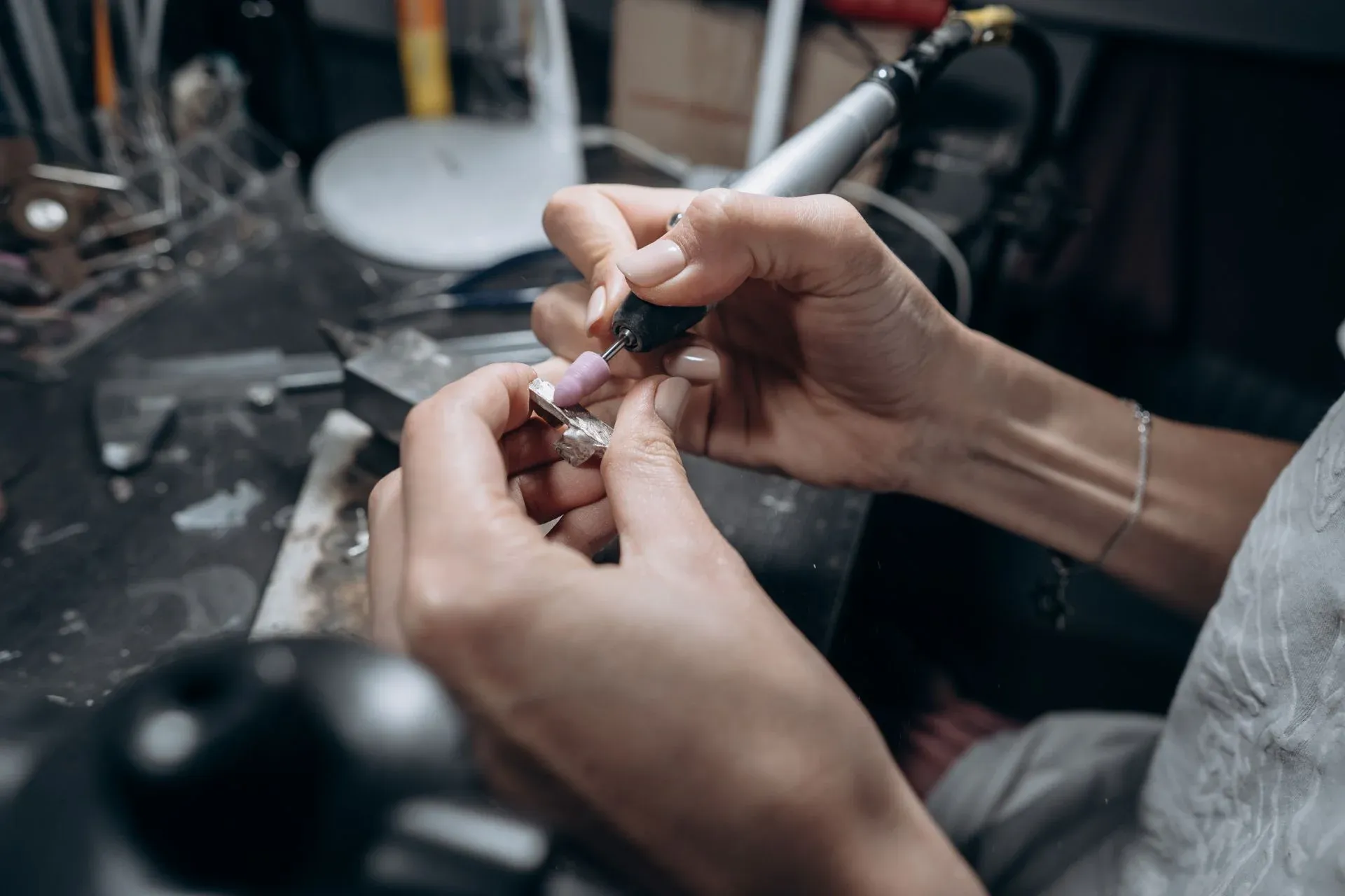 Close up of hands working on a piece of metal jewelry with a rotary tool Close up of hands working on a piece of metal jewelry with a rotary tool