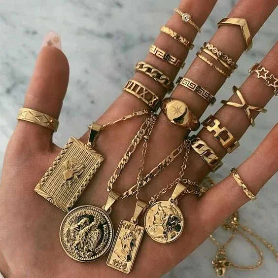 Hand adorned with multiple gold rings and holding various gold pendants Hand adorned with multiple gold rings and holding various gold pendants