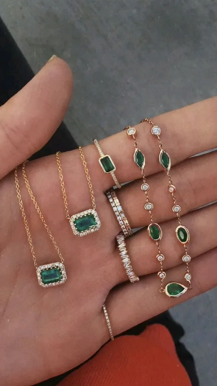 Hand holding gold jewelry with green gemstones Hand holding gold jewelry with green gemstones