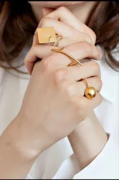 Hands clasped, wearing unique gold square and spherical rings Hands clasped, wearing unique gold square and spherical rings