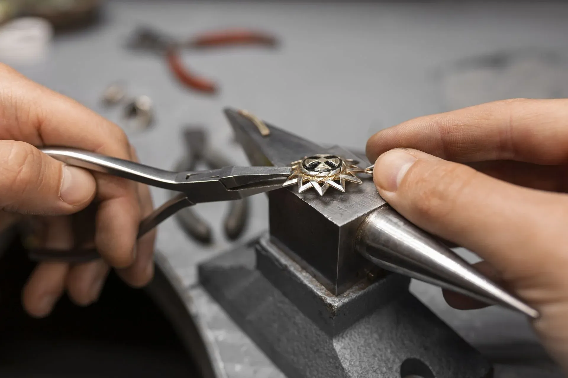 Jeweler's hands using pliers to craft a sun shaped pendant Jeweler's hands using pliers to craft a sun shaped pendant