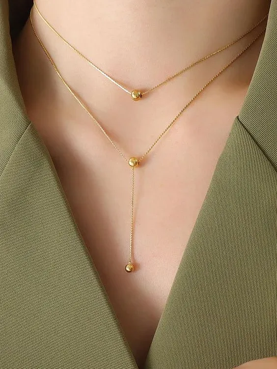 Person wearing a layered gold necklace with simple bead accents Person wearing a layered gold necklace with simple bead accents