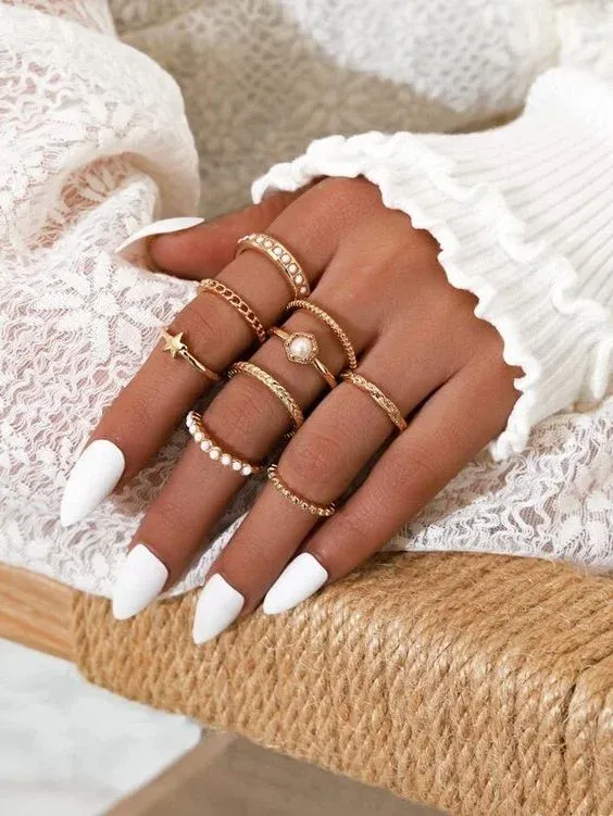 Woman's hand with white nails wearing multiple gold rings with pearls and gems Woman's hand with white nails wearing multiple gold rings with pearls and gems