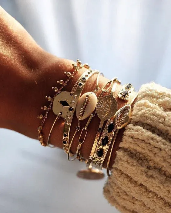 Wrist adorned with multiple gold bracelets featuring various charms Wrist adorned with multiple gold bracelets featuring various charms