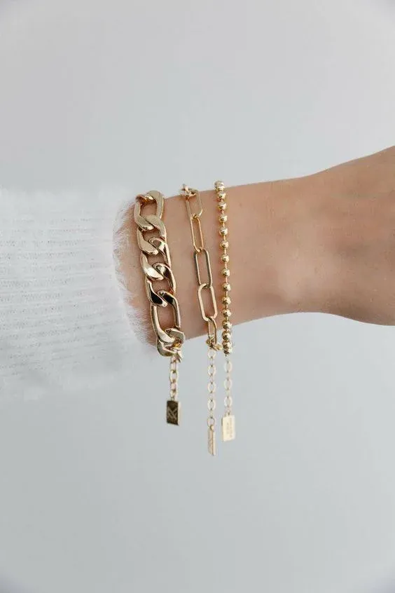 Wrist adorned with three gold bracelets in different chain styles