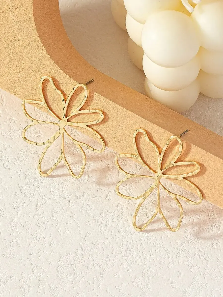 A pair of large, gold, flower shaped hoop earrings displayed on a textured surface