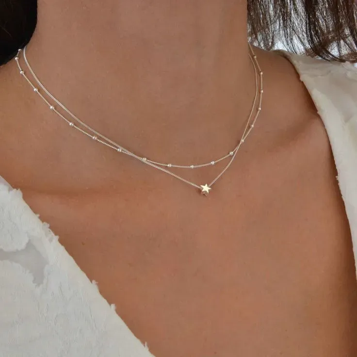Woman wearing a delicate layered necklace with a star pendant