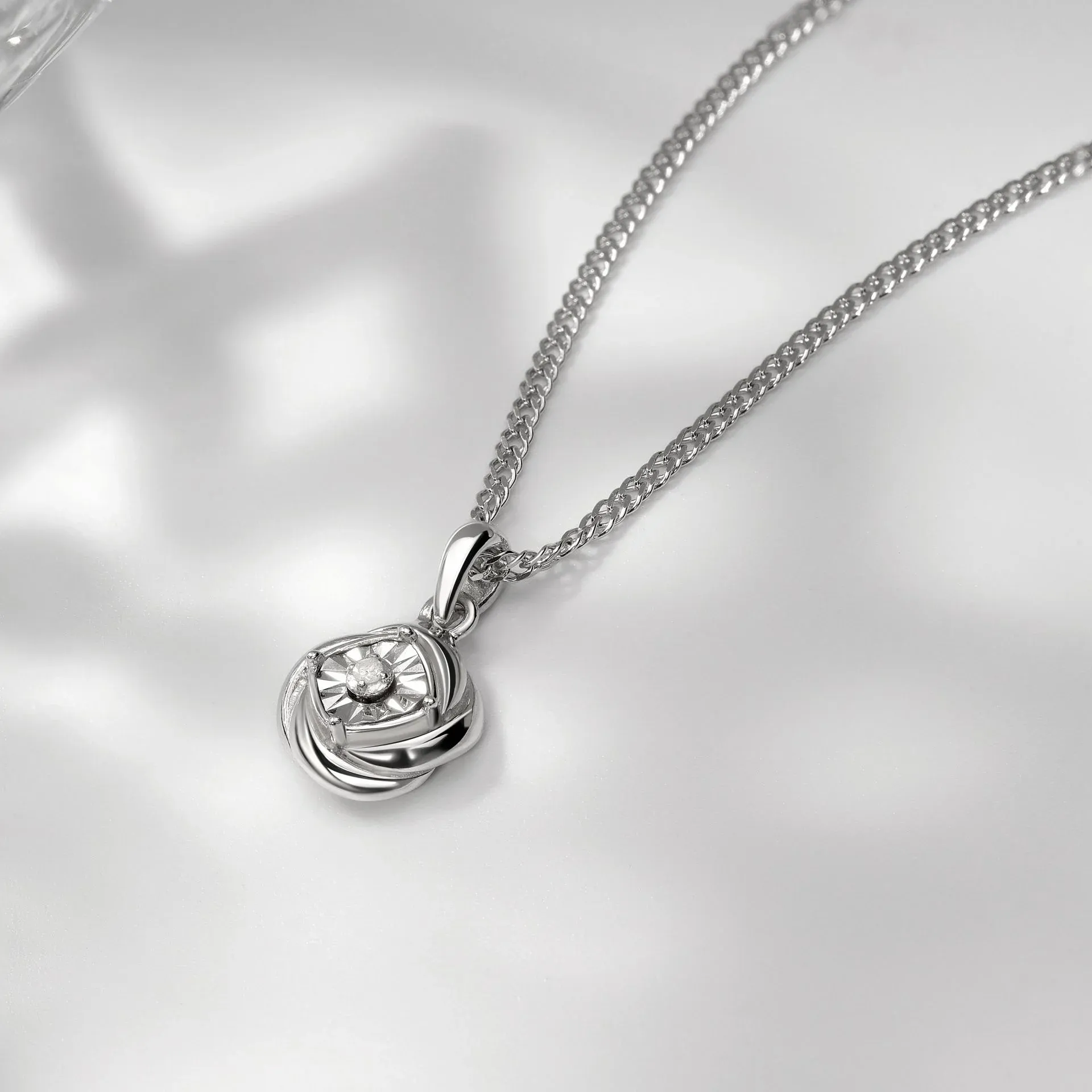 Silver necklace with a small diamond pendant on white background Silver necklace with a small diamond pendant on white background