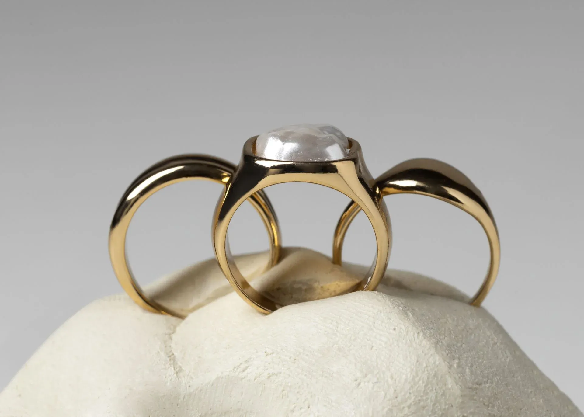 Three gold rings, one with a large pearl, resting on a white surface Three gold rings, one with a large pearl, resting on a white surface
