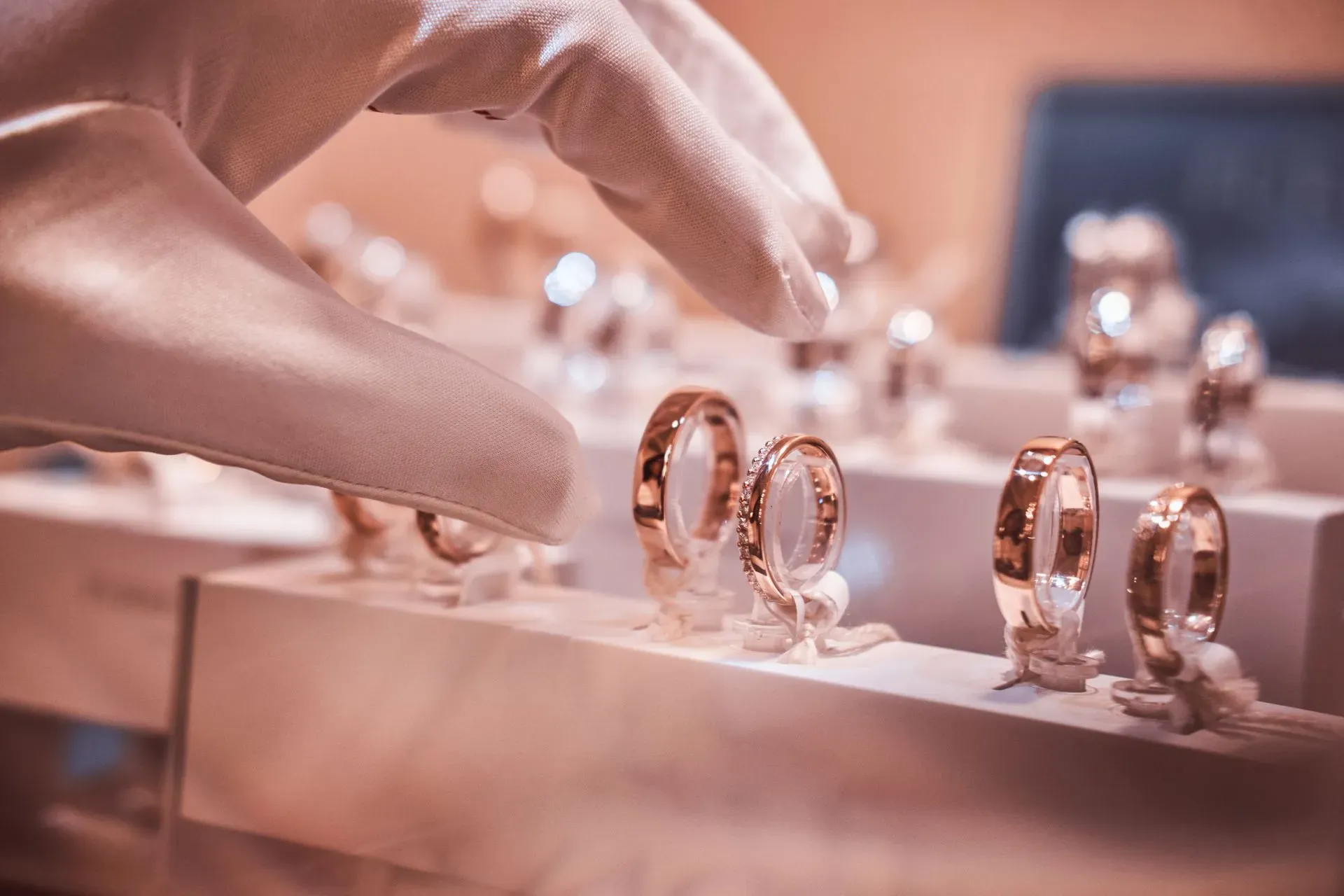 Gloved hand selecting rose gold rings from a jewelry display Gloved hand selecting rose gold rings from a jewelry display