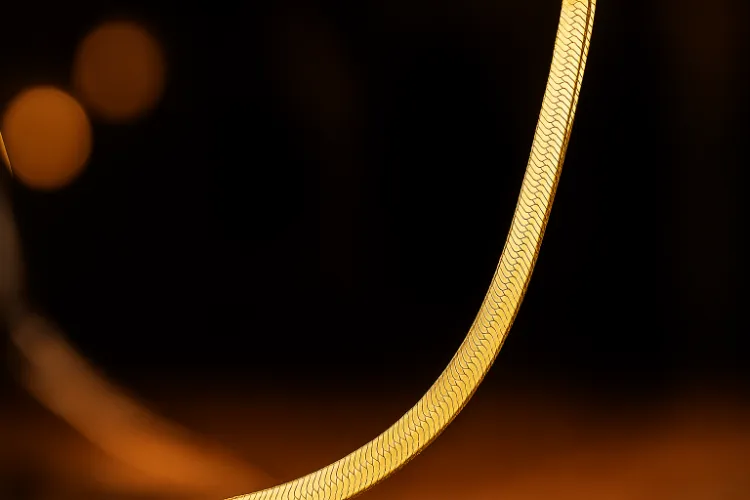 A close-up of a polished gold flat snake chain necklace, showcasing its smooth, sleek texture.