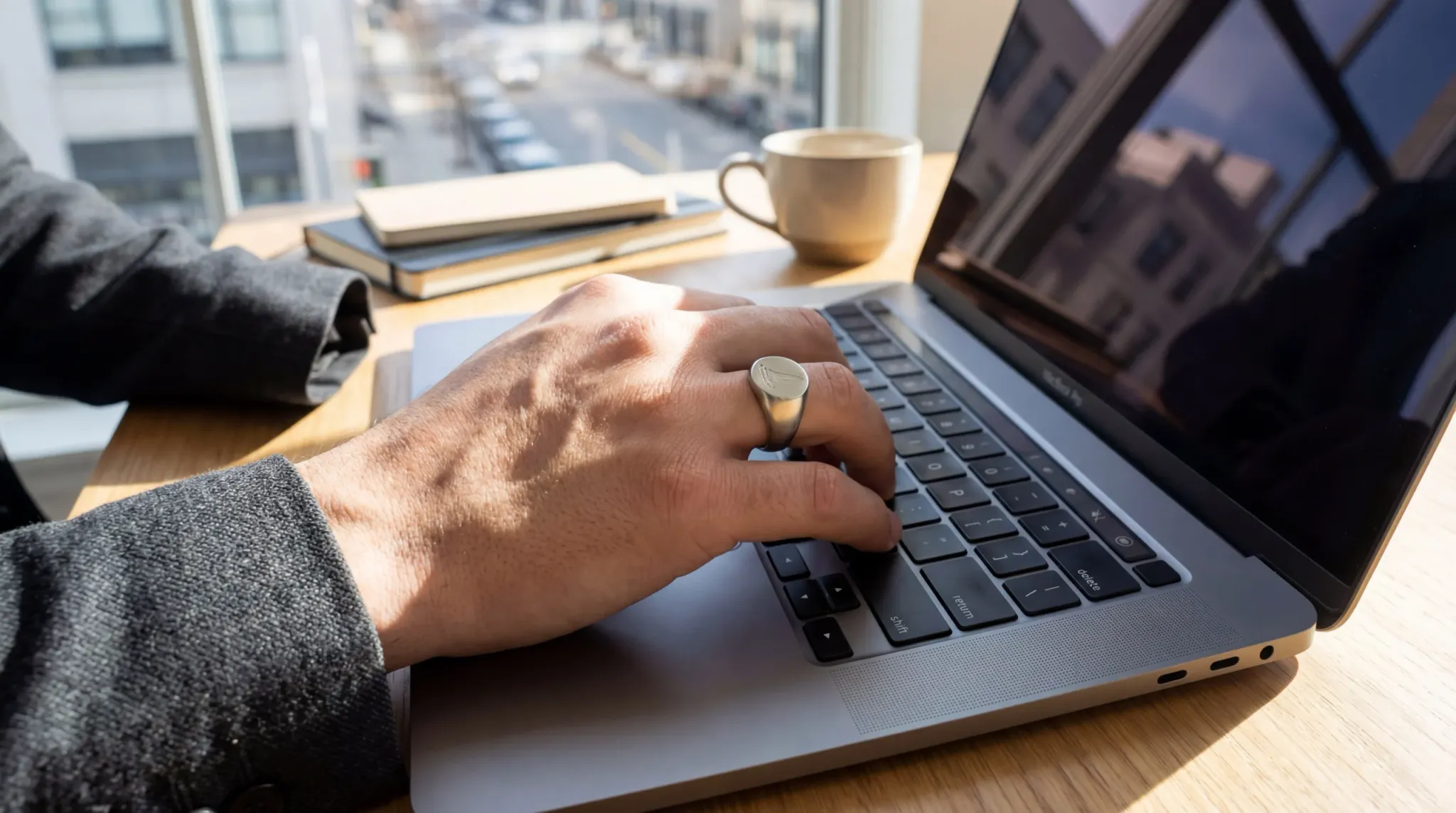 Close-up of a professional's hand wearing a sleek stainless steel signet ring while typing on a modern laptop
