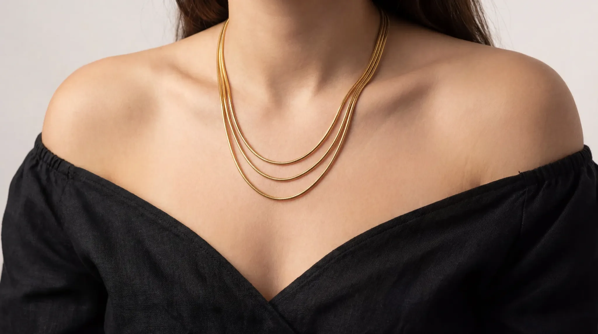 A model wearing an off-the-shoulder black dress with a three-layer 316L stainless steel gold-plated necklace set, highlighting the PVD finish.