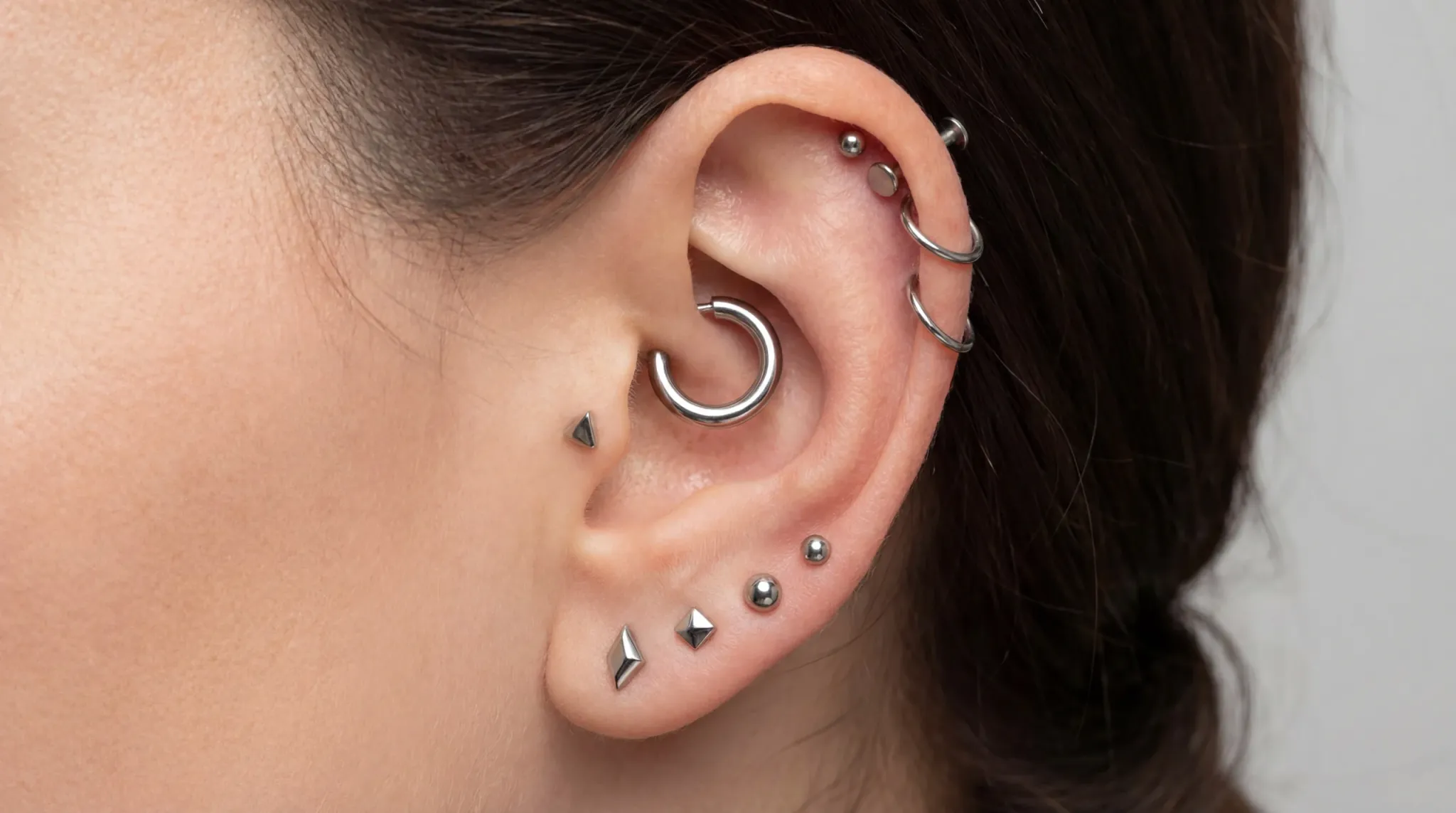 Silver ear stack piercing curation showing a conch hoop integrated with multiple lobe and helix piercings.