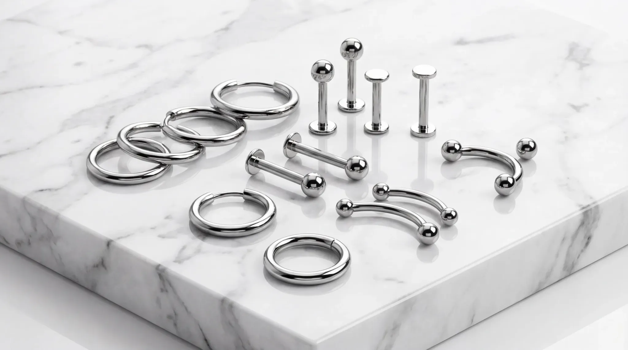 Stainless steel conch jewelry display showing various 316L studs and hoops on a marble background.
