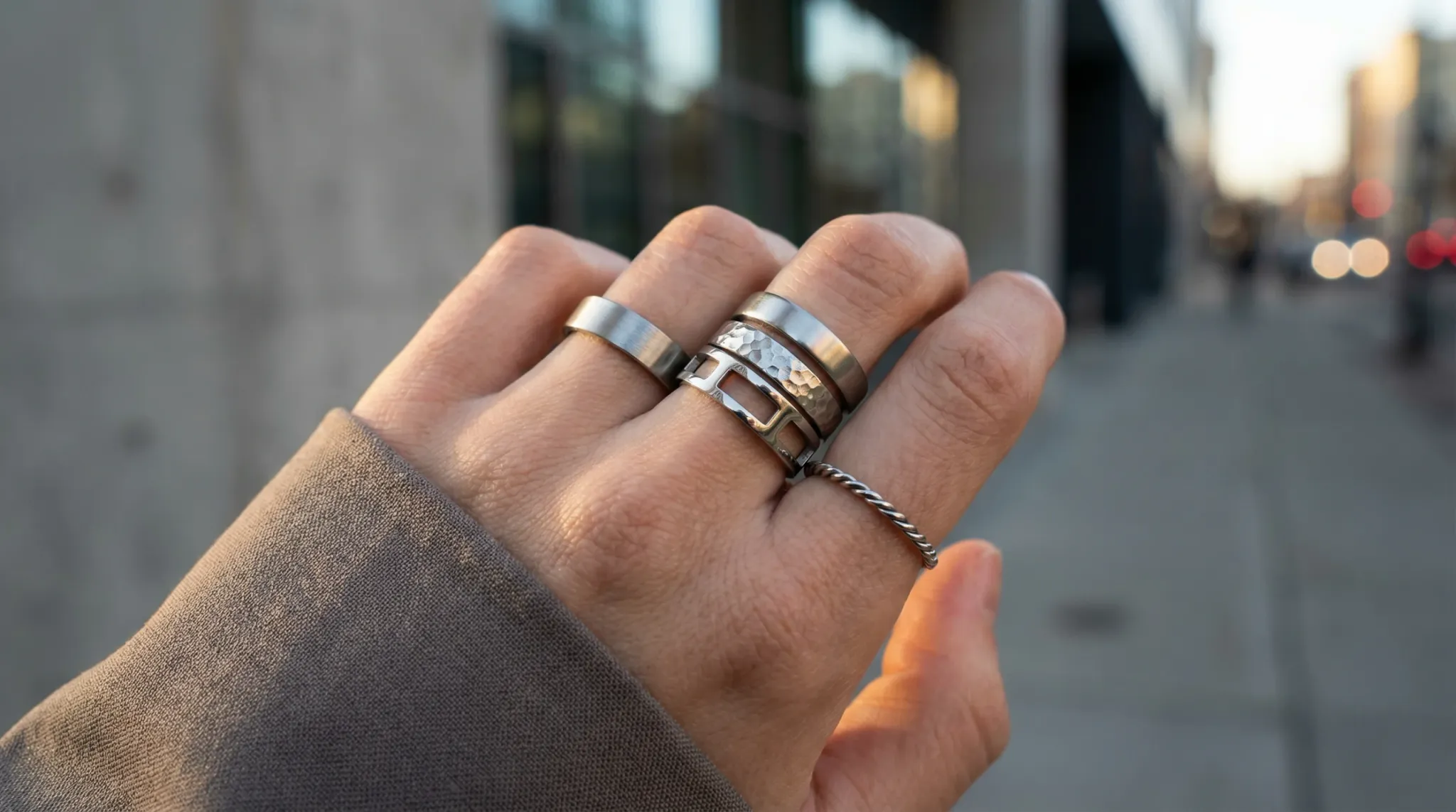 A hand showcasing the 2026 trend of layering multiple stainless steel rings with different textures.