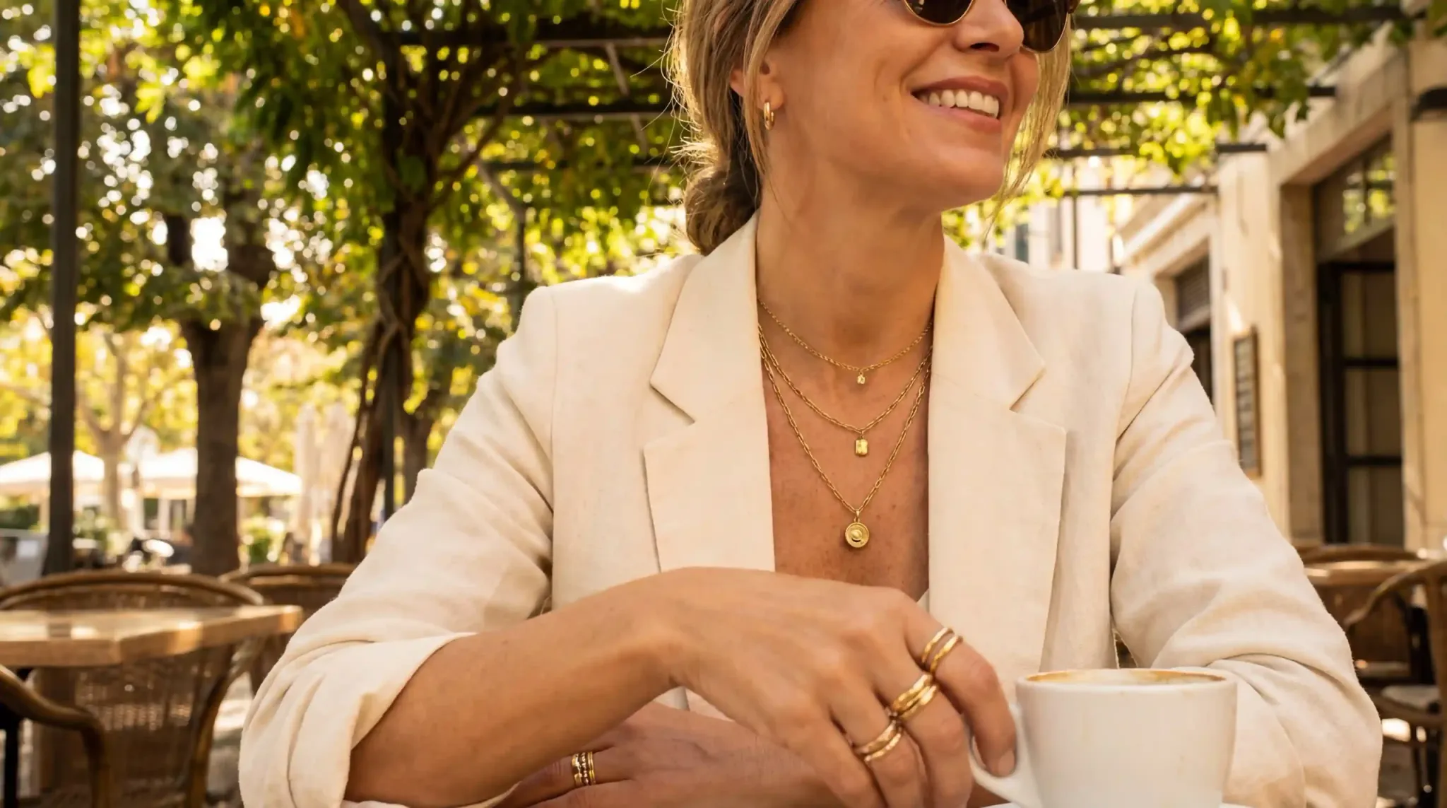 An elegant woman wearing multiple layers of 18k gold plated stainless steel jewelry at an outdoor cafe