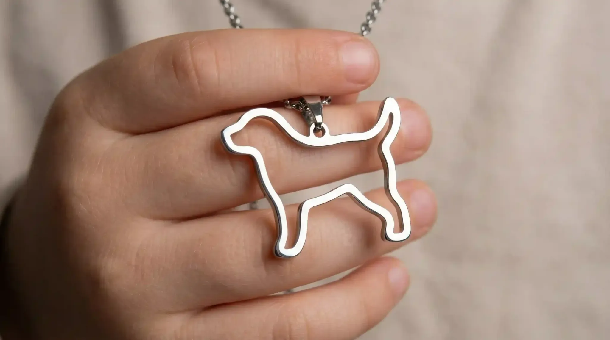 A macro shot of a polished stainless steel puppy silhouette pendant held in a child's hand.