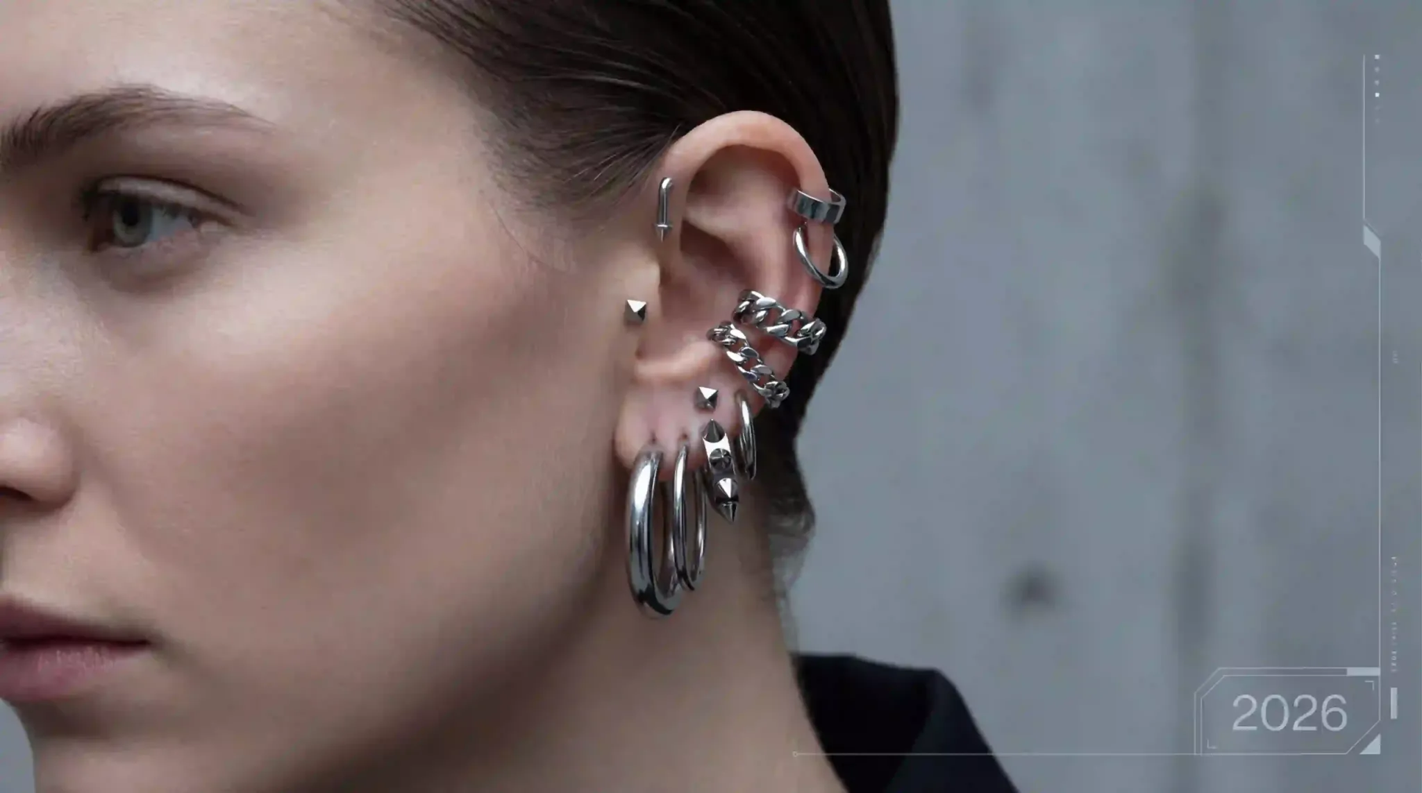 Sophisticated earring stack featuring multiple surgical-grade steel piercings, hoops, and chain links on a high-fashion model.