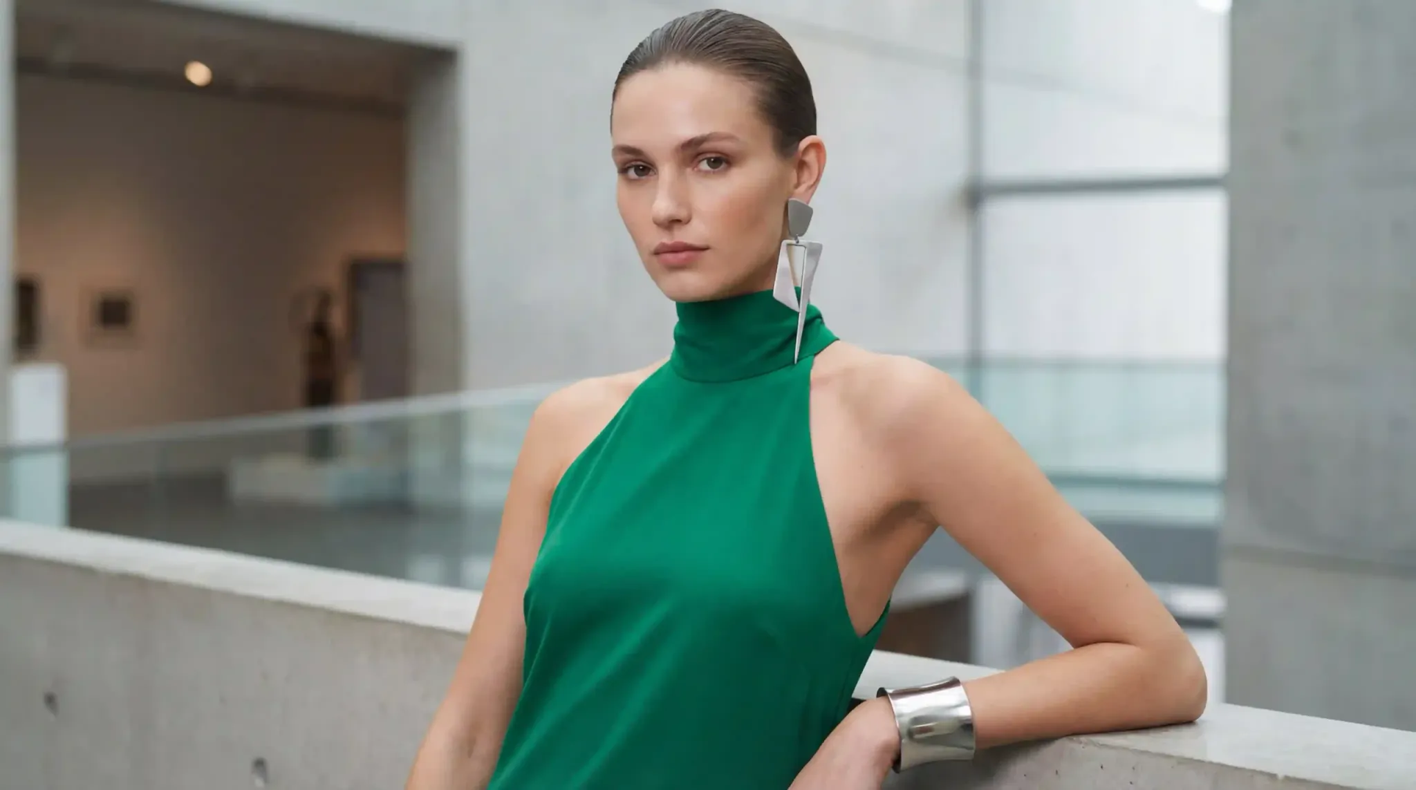 An emerald green evening gown featuring an asymmetric earring and a thick silver-tone cuff, illustrating the 2026 trend of balancing high fabric with hand accessories.