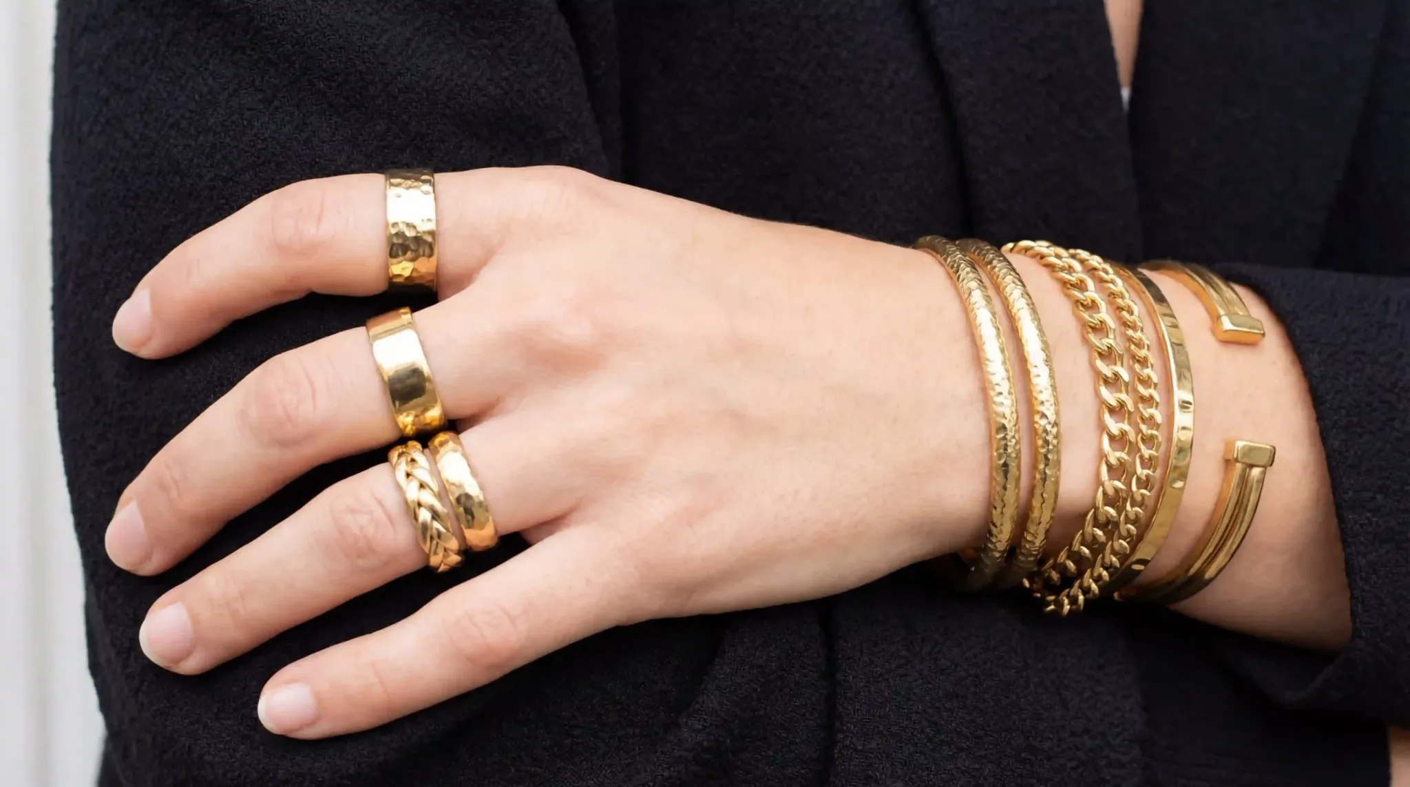 A hand showing a stack of gold-toned stainless steel rings and bracelets.