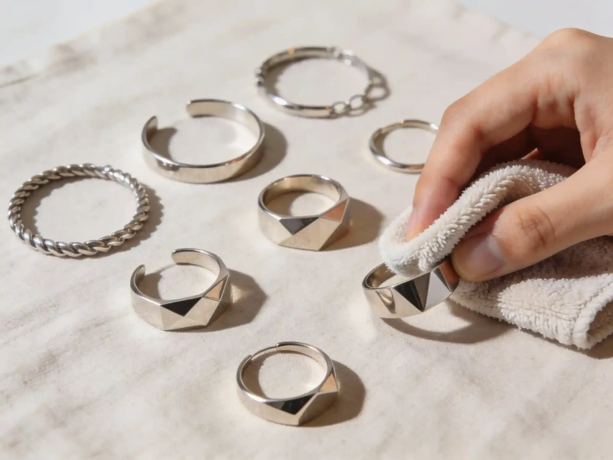 A flatlay of various stainless steel rings and bracelets being cleaned with a soft micro-fiber cloth.