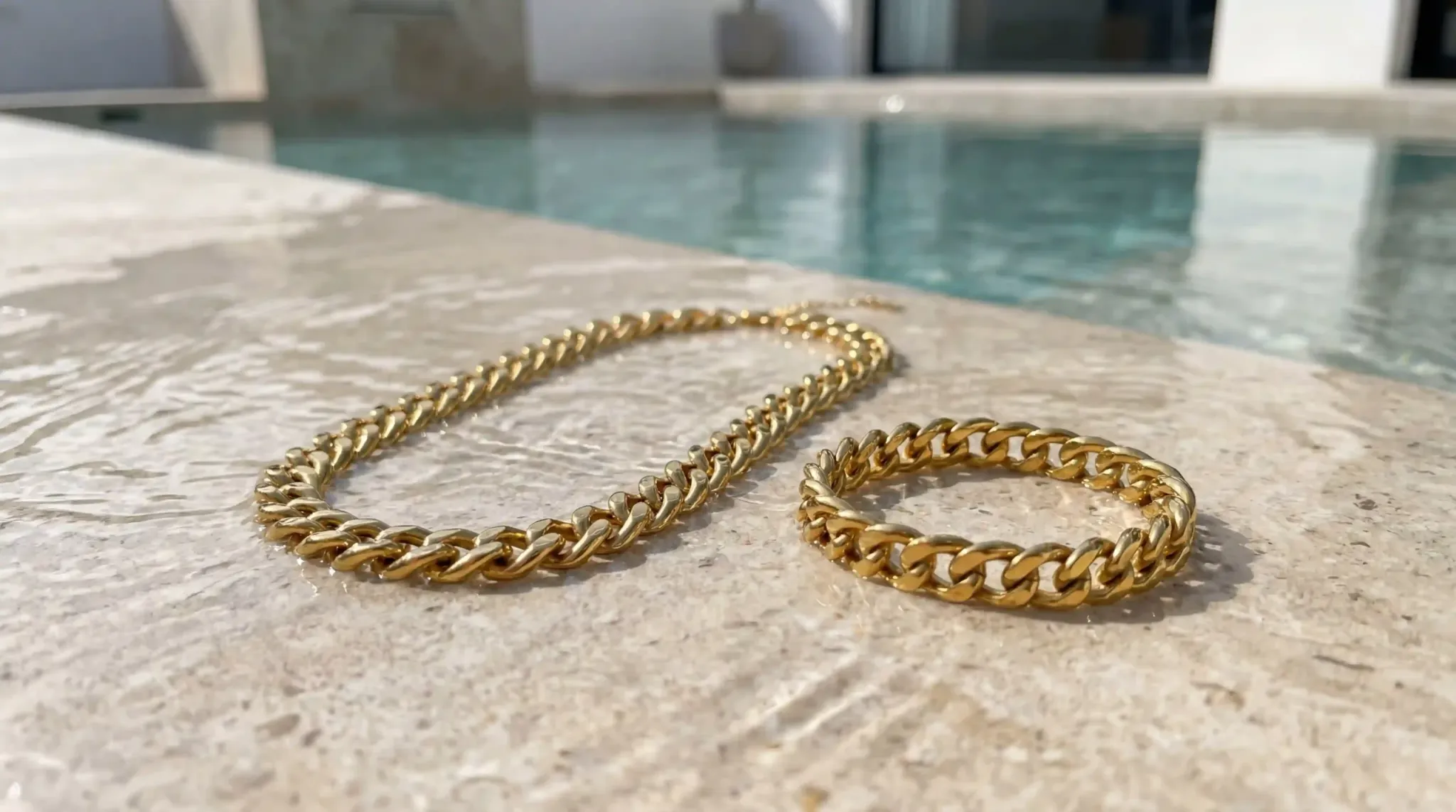 Gold stainless steel chain necklace and bracelet on a stone ledge by a pool
