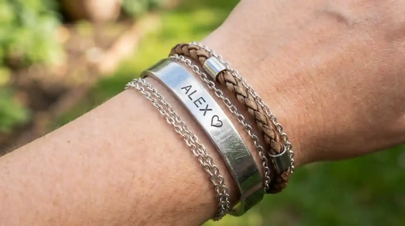 A close-up of a wrist stack featuring a personalized stainless steel name bracelet and a thin cable chain.