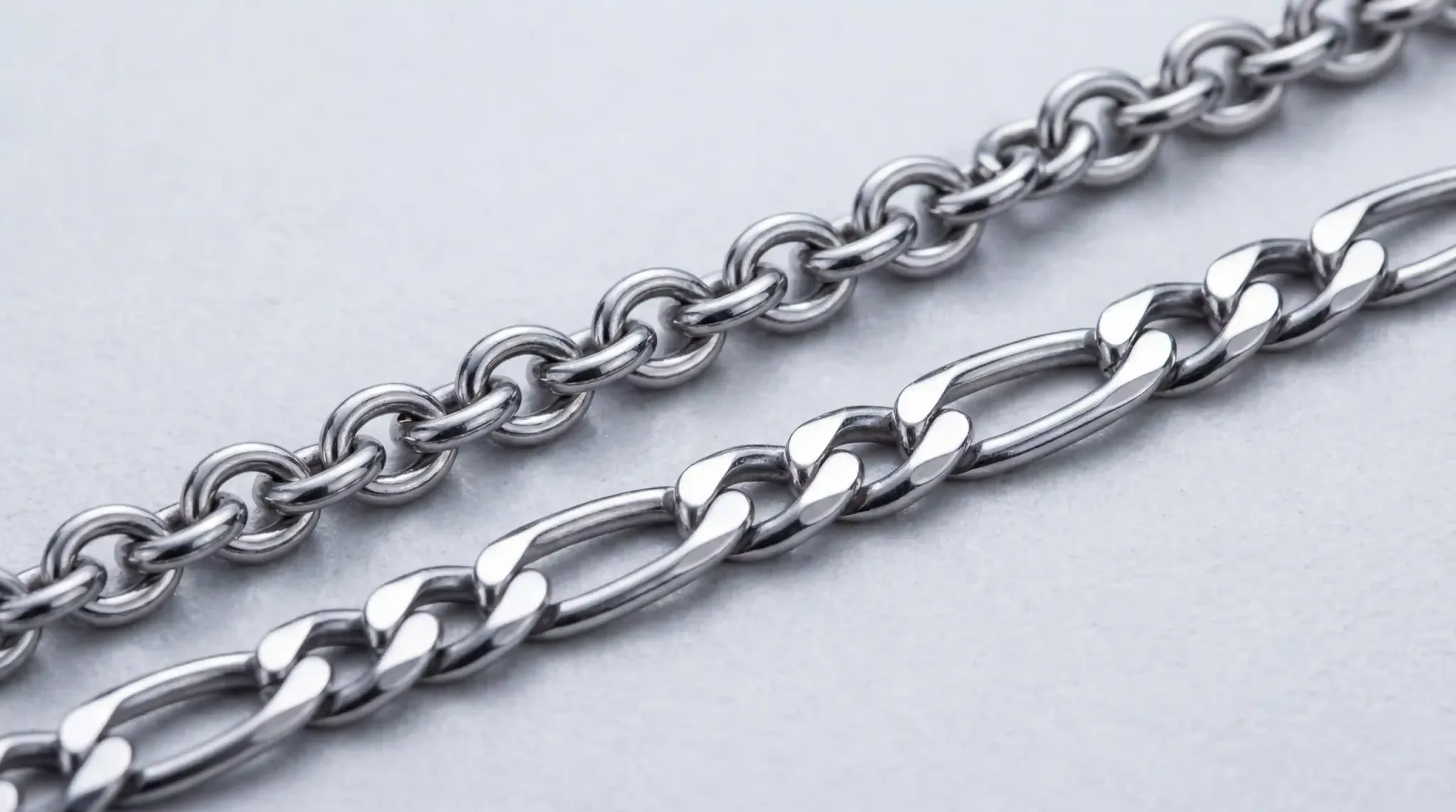 A detailed macro photography shot of 316L stainless steel cable and Figaro chains on a clean white background.