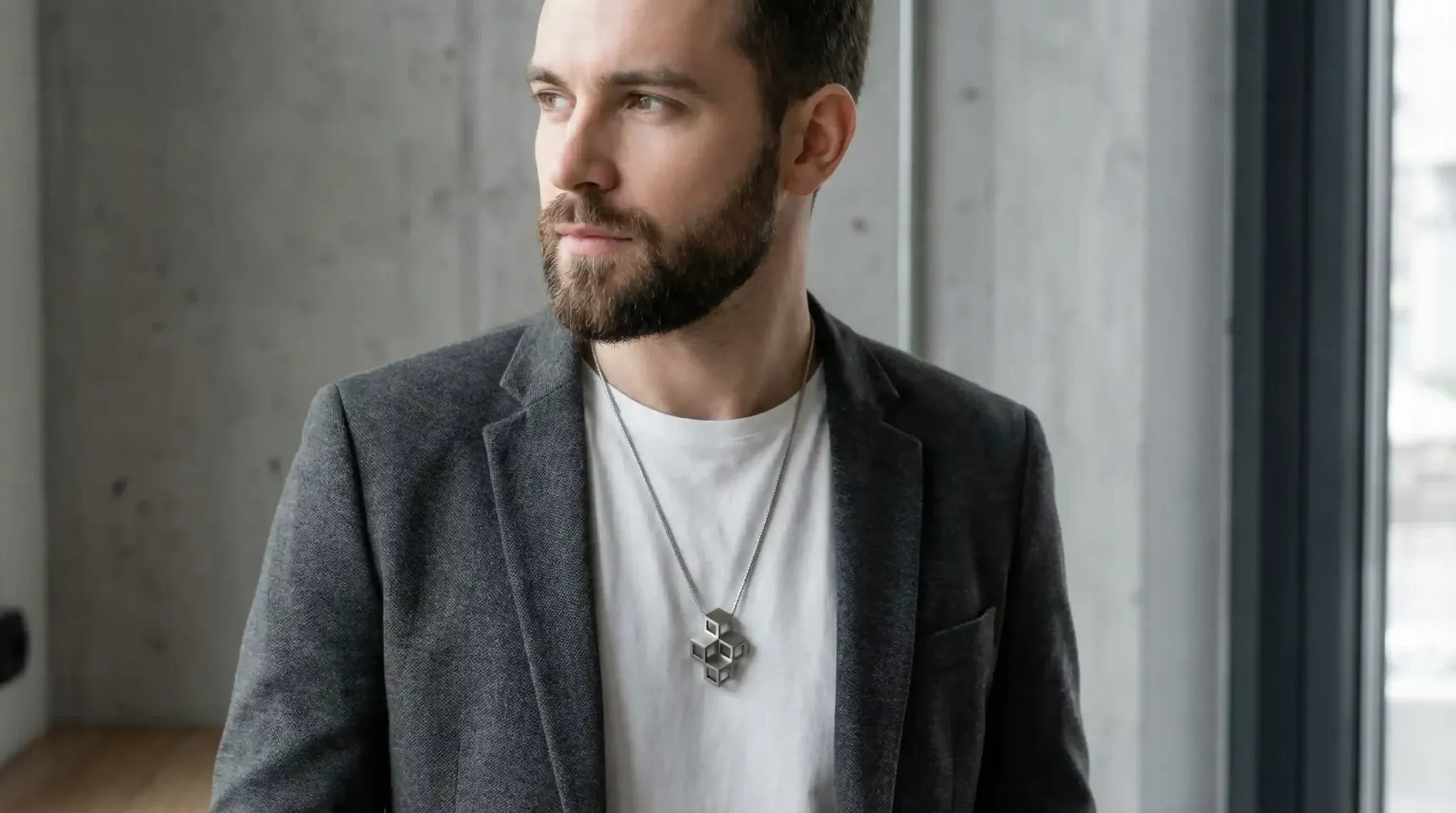 A man wearing layered stainless steel necklaces: a thin curb chain, a medium Figaro, and a small geometric pendant.